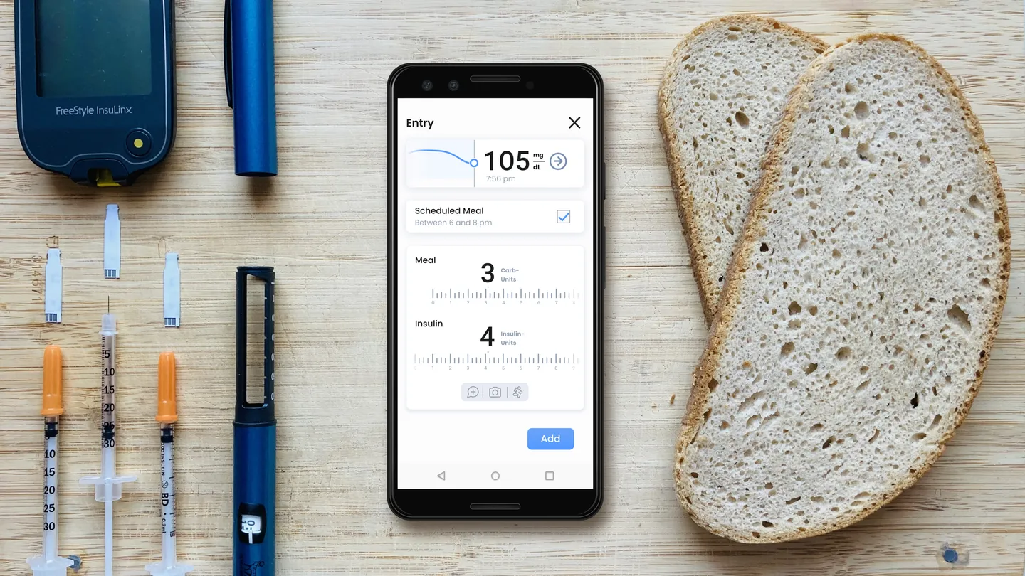 Bild: Ein Smartphone mit der App liegt auf einem Brett mit Brot und Insulinspritze