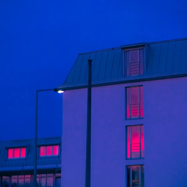 foto eines hauses in blauem licht. pinkes licht reflektiert in den fenstern